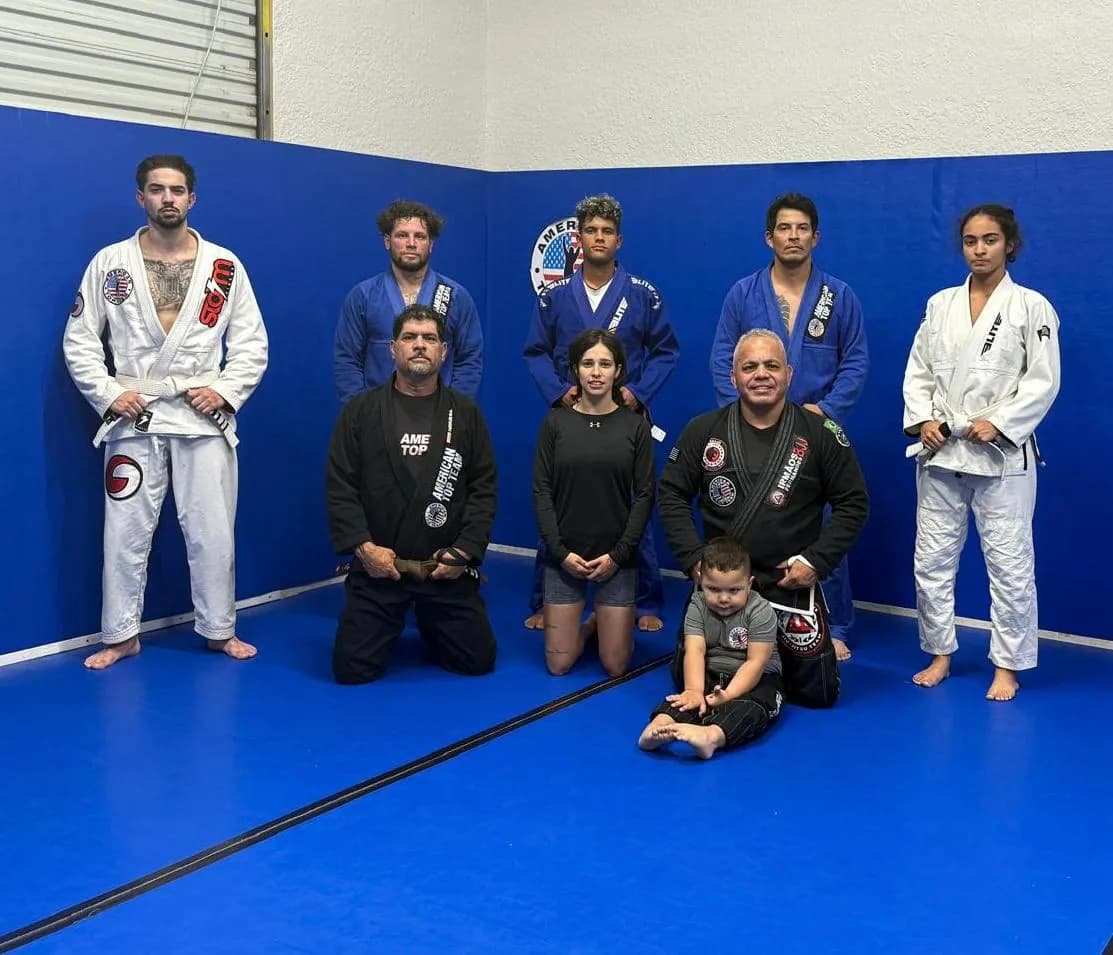 Mixed jiu-jitsu class with two women among the students, posing in gis and training clothes on blue mats with a young child in front