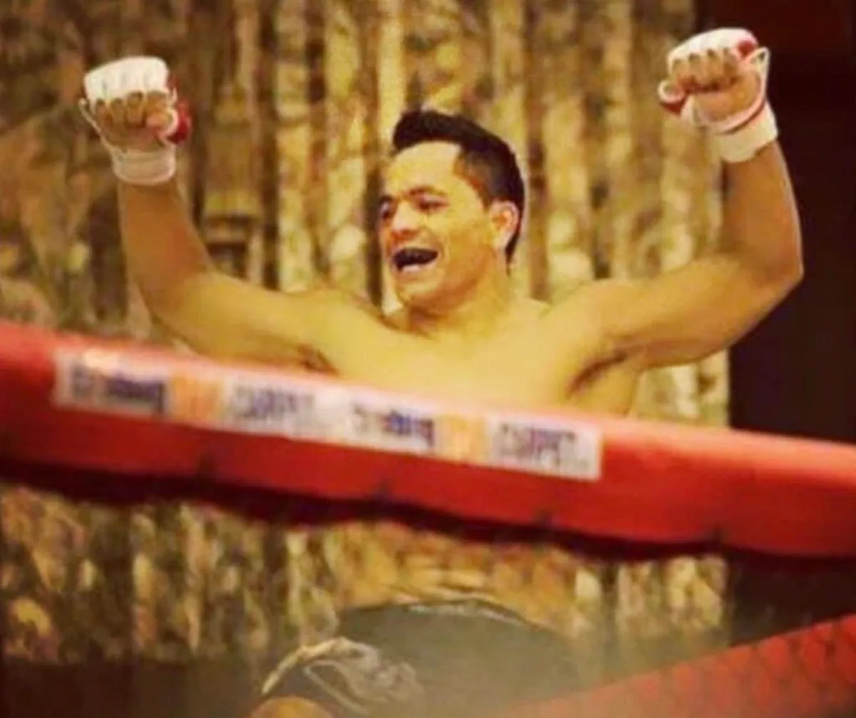 Master Willy Hardoy shirtless with taped hands, raising both arms in celebration behind the ropes of a ring